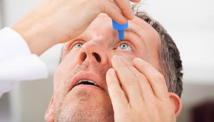 A man puts eye drops in his left eye
